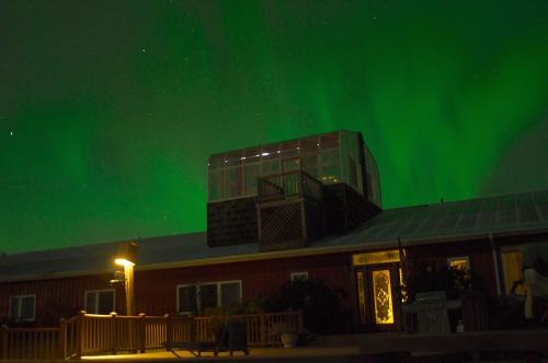 A cabin under a vibrant green aurora borealis, with a starry sky above and warm light illuminating the entrance.