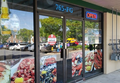 Storefront with "OPEN" sign, featuring colorful food images and a delivery sign, surrounded by parked cars.