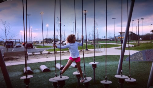 A child plays on a unique playground structure with ropes and platforms, set against a twilight sky.