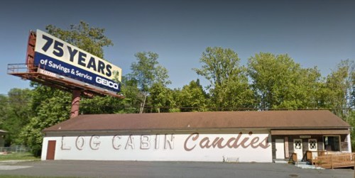 A building with "Log Cabin Candies" painted on it, under a billboard celebrating 75 years of GEICO savings and service.