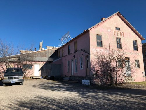 A pink building with a sign reading "Home of Peat" and a parked truck in front, under a clear blue sky.