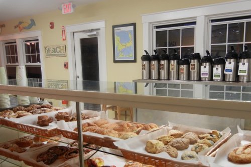 A display case filled with various baked goods, with coffee dispensers and a map on the wall in a cozy café setting.