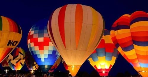 Colorful hot air balloons illuminated at night, creating a vibrant display against a dark sky.