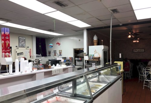 Interior of an ice cream shop with a service counter, ice cream display, and seating area in a cozy atmosphere.