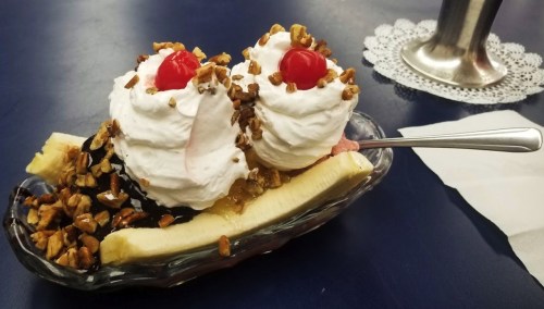 A banana split topped with whipped cream, cherries, and chopped nuts, served in a glass dish.