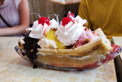 A colorful banana split topped with whipped cream, cherries, and various ice cream flavors in a glass dish.