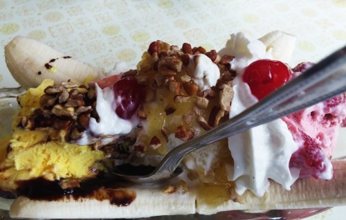 A banana split topped with ice cream, whipped cream, nuts, cherries, and chocolate sauce in a glass dish.