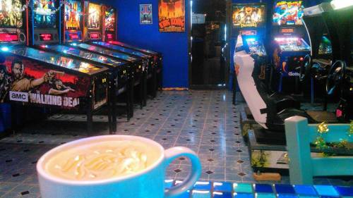 A cozy café scene featuring a cup of coffee in the foreground and a vibrant arcade with pinball machines in the background.