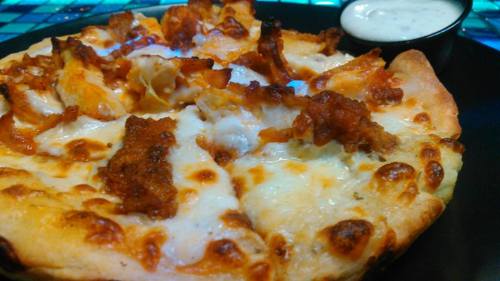 A close-up of a cheesy pizza topped with crispy chicken pieces, served with a side of ranch dressing.