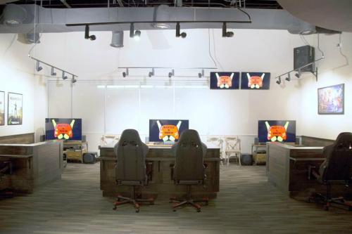 A modern office space with four gaming chairs, desks, and multiple screens displaying cartoon characters.