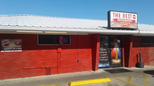 Exterior of "The Best Supermarket," featuring a red brick facade, open sign, and a mural on the door.