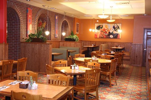 Cozy restaurant interior with wooden tables, chairs, and colorful decor, featuring plants and artwork on the walls.