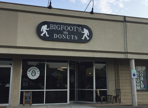 Exterior of a donut shop named "Bigfoot's Little Donuts," featuring a sign with a Bigfoot silhouette.