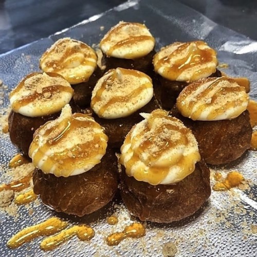 A plate of small, round pastries topped with cream, caramel drizzle, and a sprinkle of crumbs.