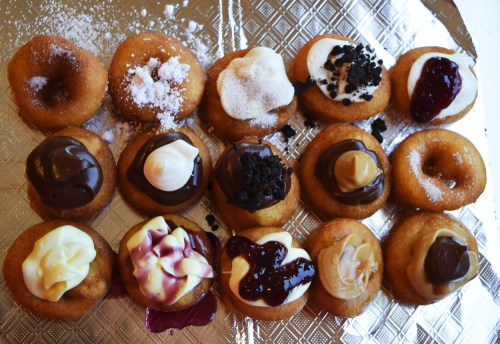 A tray of mini donuts topped with various frostings, including chocolate, cream, and fruit sauces.