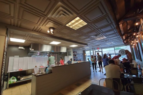 A busy restaurant interior with a counter, kitchen area, and customers waiting in line. Bright and inviting atmosphere.