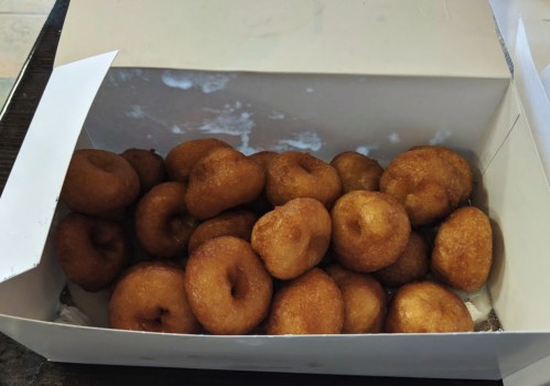 A white box filled with golden-brown, freshly made mini donuts.