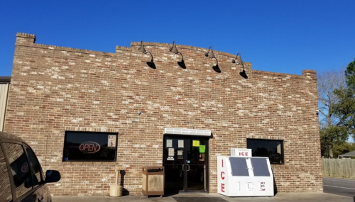 A brick building with an "OPEN" sign and an ice vending machine in front, under a clear blue sky.