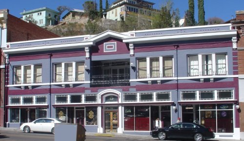 Historic two-story building with purple and gray exterior, featuring large windows and a balcony, set in a quaint street.