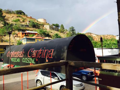 A colorful restaurant sign for "Cortessa's Cantina" with a rainbow in the background and hills in the distance.