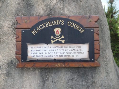 Sign about Blackbeard's Course, detailing his iconic black beard and battle attire, including pigtails and fuse cord.