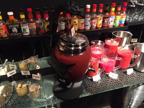 A bar setup featuring a large drink dispenser, colorful beverages, and various hot sauce bottles in the background.