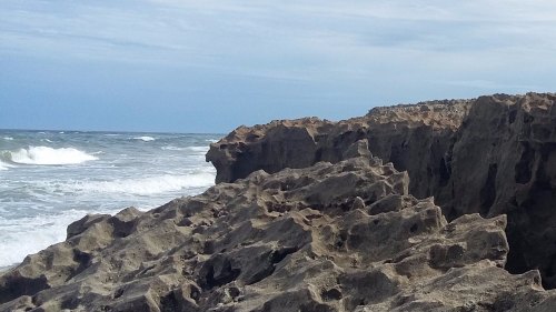 Rocky coastline with waves crashing against the shore under a cloudy sky.