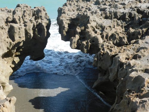 Rocky formations frame a view of waves crashing on a sandy beach, with turquoise water in the background.