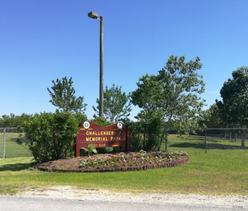 Sign for Challenger Memorial Park surrounded by greenery and flowers under a clear blue sky.