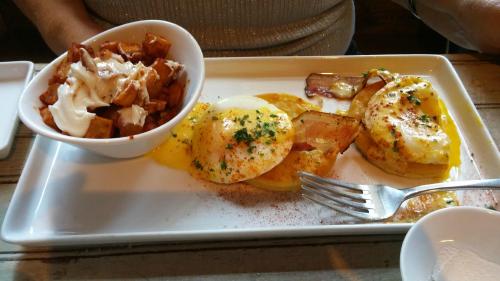 A plate of eggs Benedict with potatoes and a side of creamy sauce, served on a white rectangular dish.