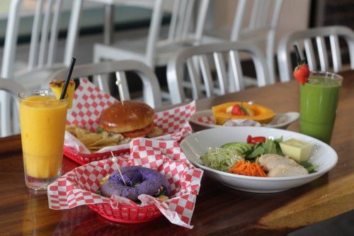A colorful spread of food including a burger, fries, salads, and drinks on a wooden table with checkered baskets.