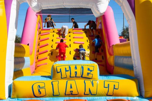 Children climbing an inflatable obstacle course labeled "THE GIANT" on a sunny day.
