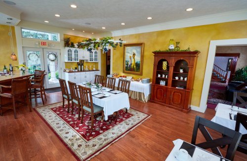 Cozy restaurant interior with wooden tables, chairs, and warm yellow walls, featuring a buffet area and decorative plants.