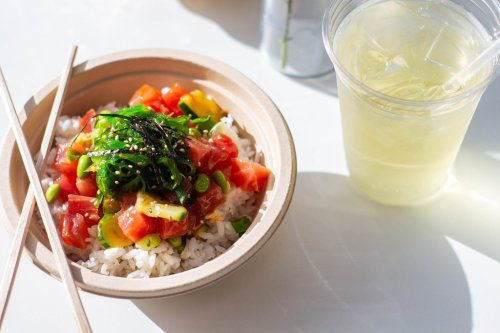 A bowl of rice topped with diced vegetables and seaweed, alongside a cup of iced green tea.