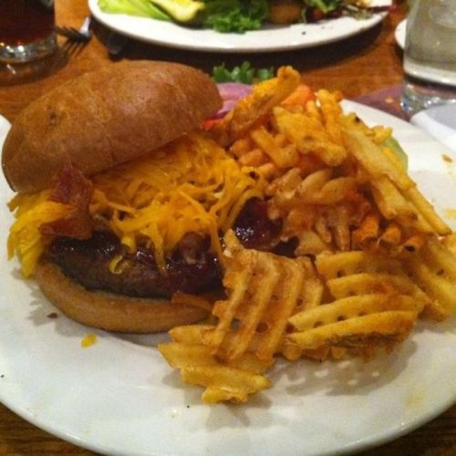 A hearty burger topped with melted cheese and bacon, served with a side of crispy waffle fries on a white plate.