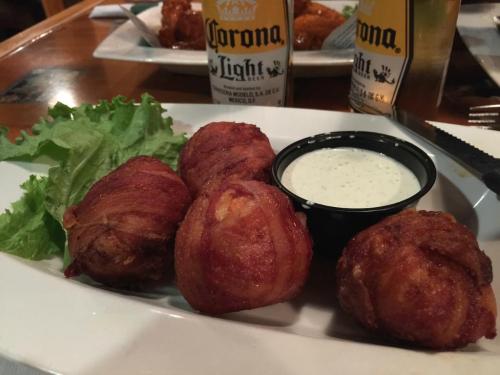 Four bacon-wrapped balls on a plate with lettuce and a small cup of dipping sauce, alongside two bottles of beer.