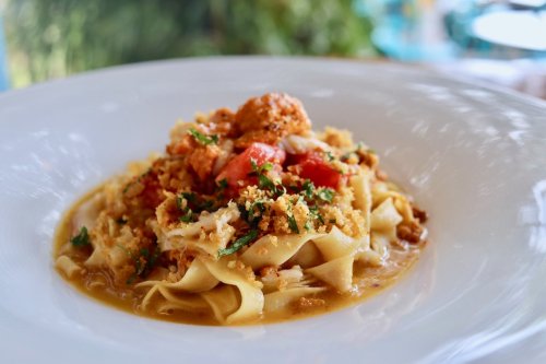 A plate of pasta topped with tomatoes, herbs, and breadcrumbs, served in a light sauce.