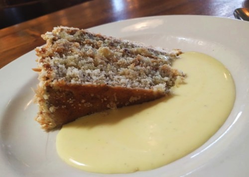 A slice of cake on a plate with a creamy yellow sauce beside it.