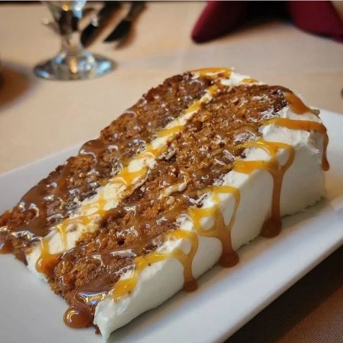 A slice of cake topped with creamy frosting and drizzled with caramel sauce, served on a white plate.