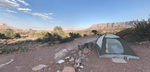 A tent set up on rocky terrain, surrounded by desert landscape and distant mountains under a clear blue sky.