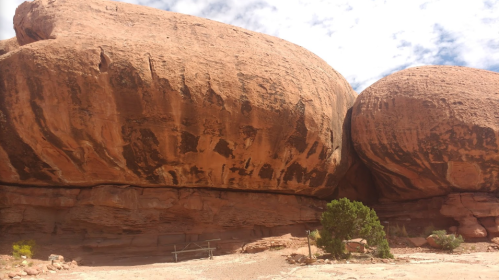 Two large, rounded rock formations under a cloudy sky, with sparse vegetation and a small structure in the foreground.