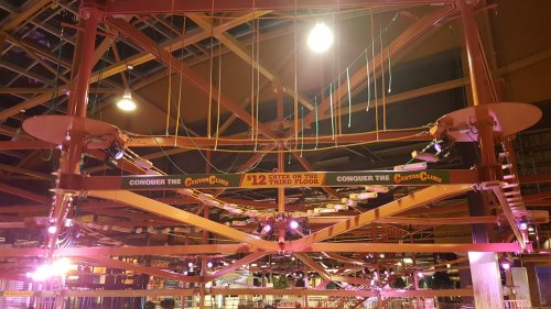 A brightly lit indoor amusement area with a sign reading "Conquer the Third Floor" and colorful structures overhead.