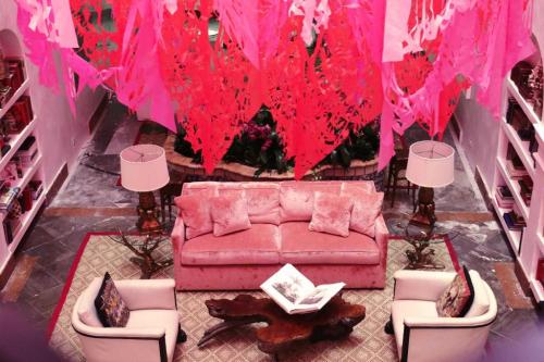 A cozy living room with a pink sofa, white chairs, and vibrant pink decorations hanging from the ceiling.
