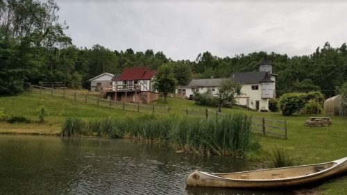 A serene landscape featuring a pond, a canoe, and several houses surrounded by greenery and trees.