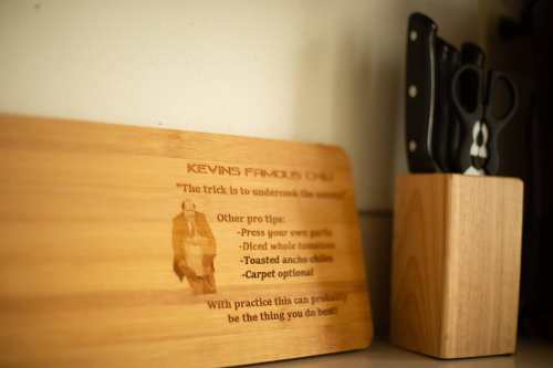 A wooden cutting board with cooking tips and a knife block with scissors in the background.