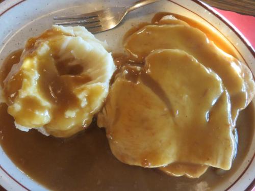 A plate of mashed potatoes topped with gravy, alongside slices of chicken smothered in brown gravy.