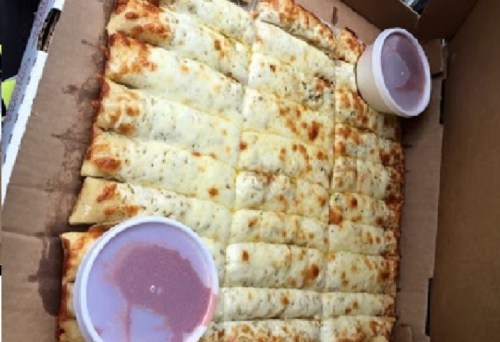 A pizza box filled with cheesy breadsticks, served with two cups of marinara sauce on the side.