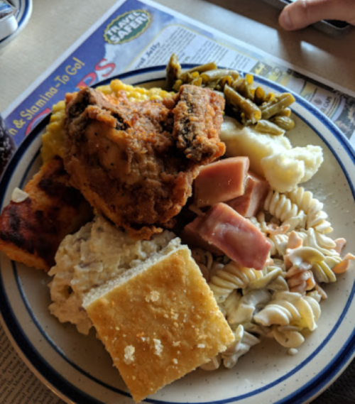 A plate of fried chicken, cornbread, pasta salad, green beans, mashed potatoes, and ham.