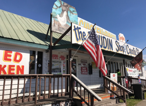 A colorful storefront with a large sign, an American flag, and various menu boards outside.
