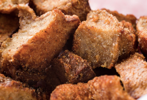 Close-up of crispy, golden-brown pieces of fried pork, seasoned and stacked together.